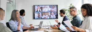 Diverse company employees having online business conference video call on tv screen monitor in board meeting room. Videoconference presentation, global virtual group corporate training concept. (Diverse company employees having online business confere